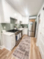 home renovation near cornelius NC featuring a renovated kitchen with light green glass subway tile backsplash. ligth wood floors, white cabinetry and stainless appliances finish the look.