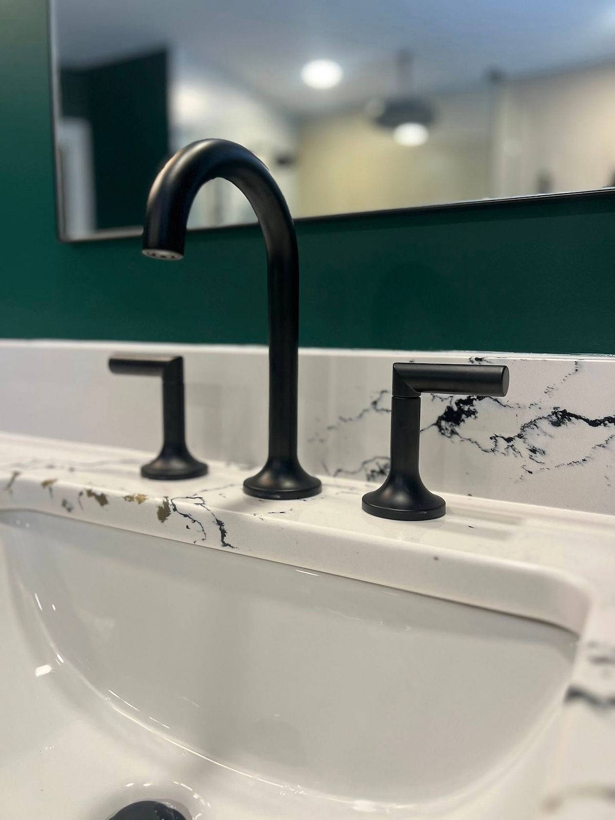 Black faucet set on marble countertop with gray veins. Green wall and mirror in background. Modern and sleek bathroom design in home renovation near Cornelius, NC.