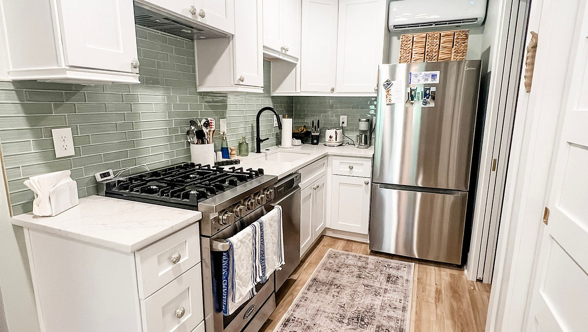 home renovation near Cornelius, NC featuring a renovated kitchen with light wood flooring, white cabinetry, and blue-green glass tile backsplash.