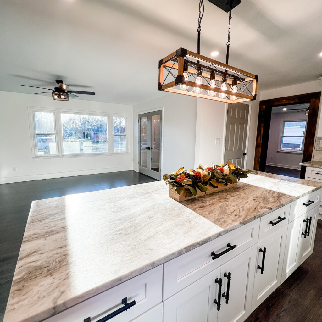 home renovation near Davidson, NC featuring oversized kitchen island with stone countertops, a floral arrangement in the middle, and a farmhouse style light fixture hanging above.