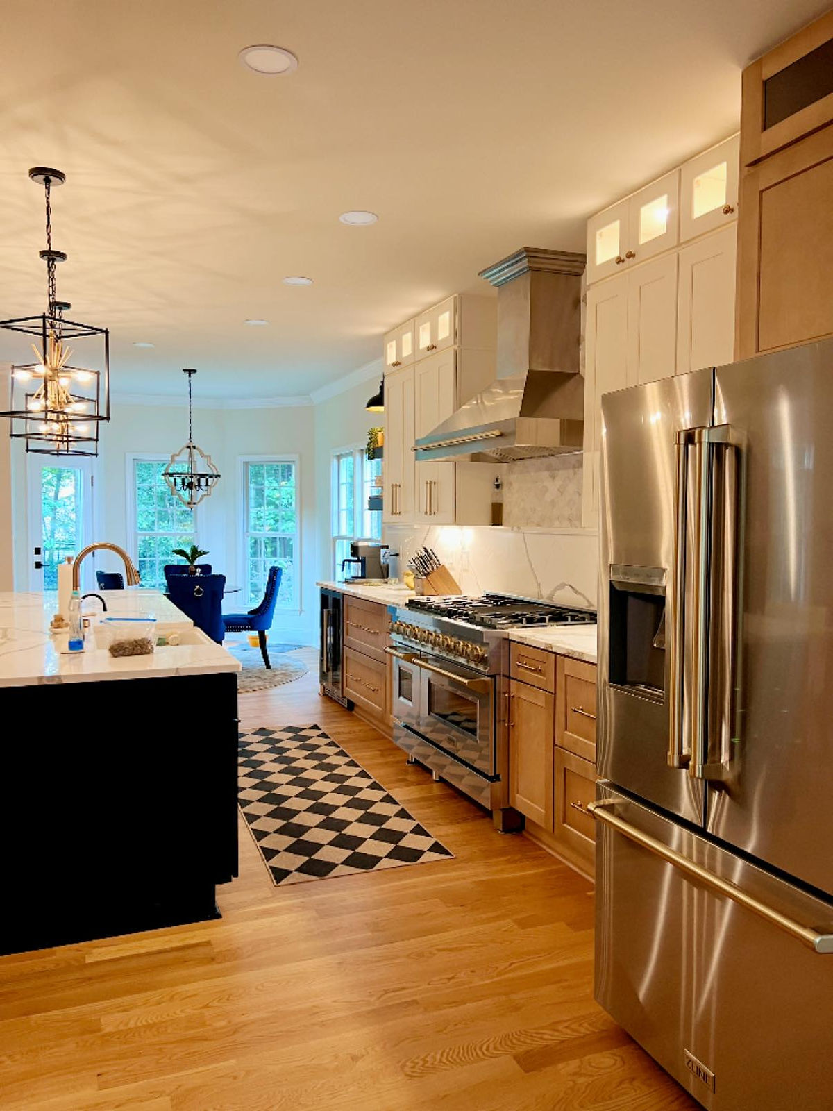 Modern kitchen with stainless steel appliances, wood cabinets, and marble countertops. A checkered rug on wood floor, bright dining area complete this kitchen renovation near Huntersville, NC.
