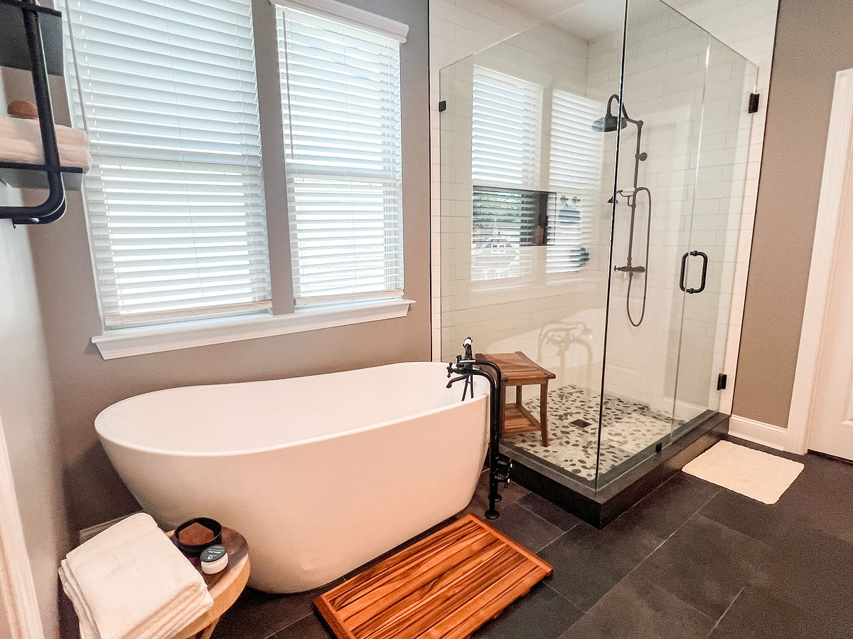 renovated bathroom with tan walls, pebble tile shower floor, soaking tub, and teak bathmat