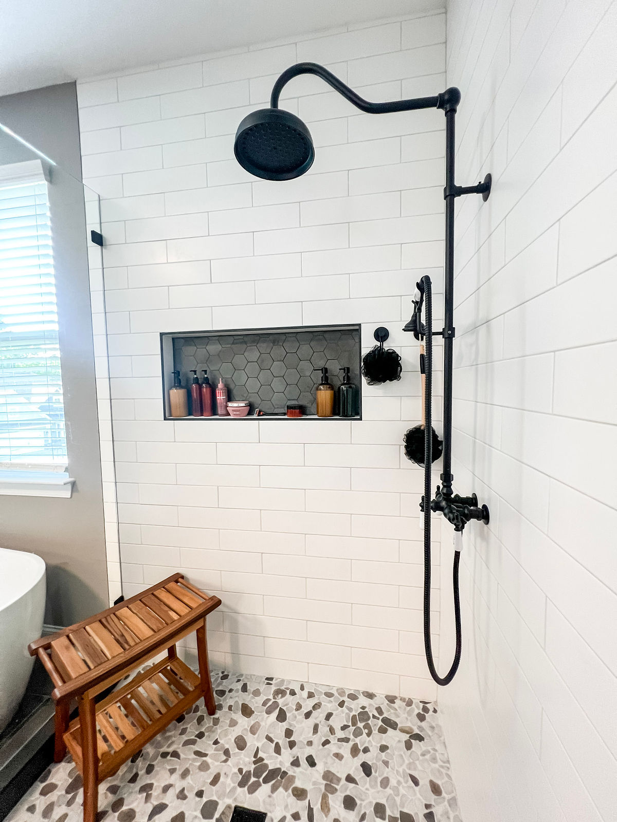 home renovation near Huntersville, NC featuring renovated bathroom with white subway tile shower, gray hex tile inside decorative storage niche and black hardware.