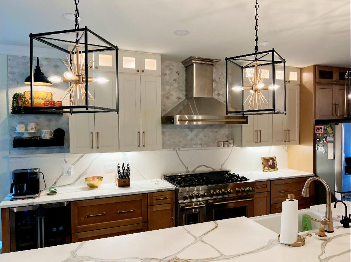 Modern kitchen with marble countertops, stainless steel stove hood, and geometric pendant lights. Warm wood cabinets, white accents. Kitchen Renovation near Huntersville, NC.