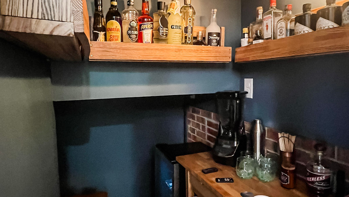 home renovation near Huntersville, NC featuring an under staircase bar painted a moody gray with open natural shelving and a wine cooler in the back corner.