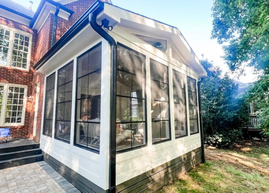 A sun room creates an amazing weekend living space in NC. Black framed windows in white siding surround the exterior of this new three season porch.