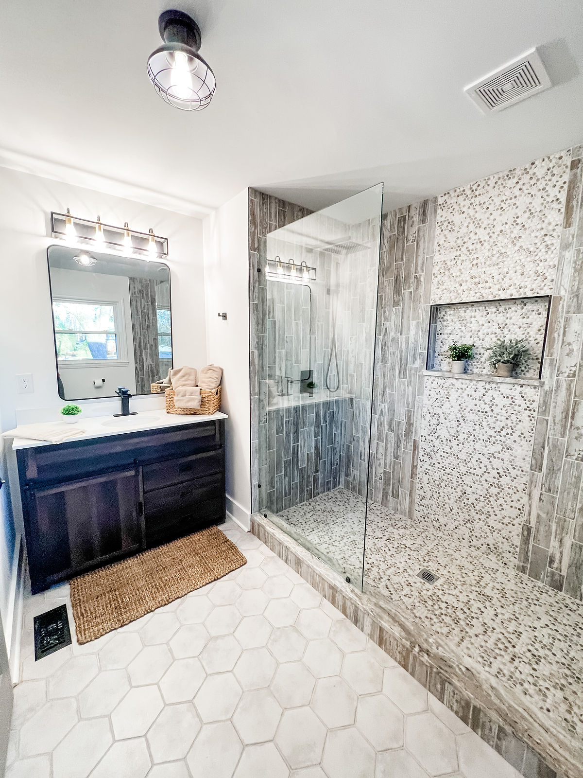 bathroom renovation featuring fully tiled shower with decorative accent and insert. light colored hex tile flooring and a dark vanity cabinet