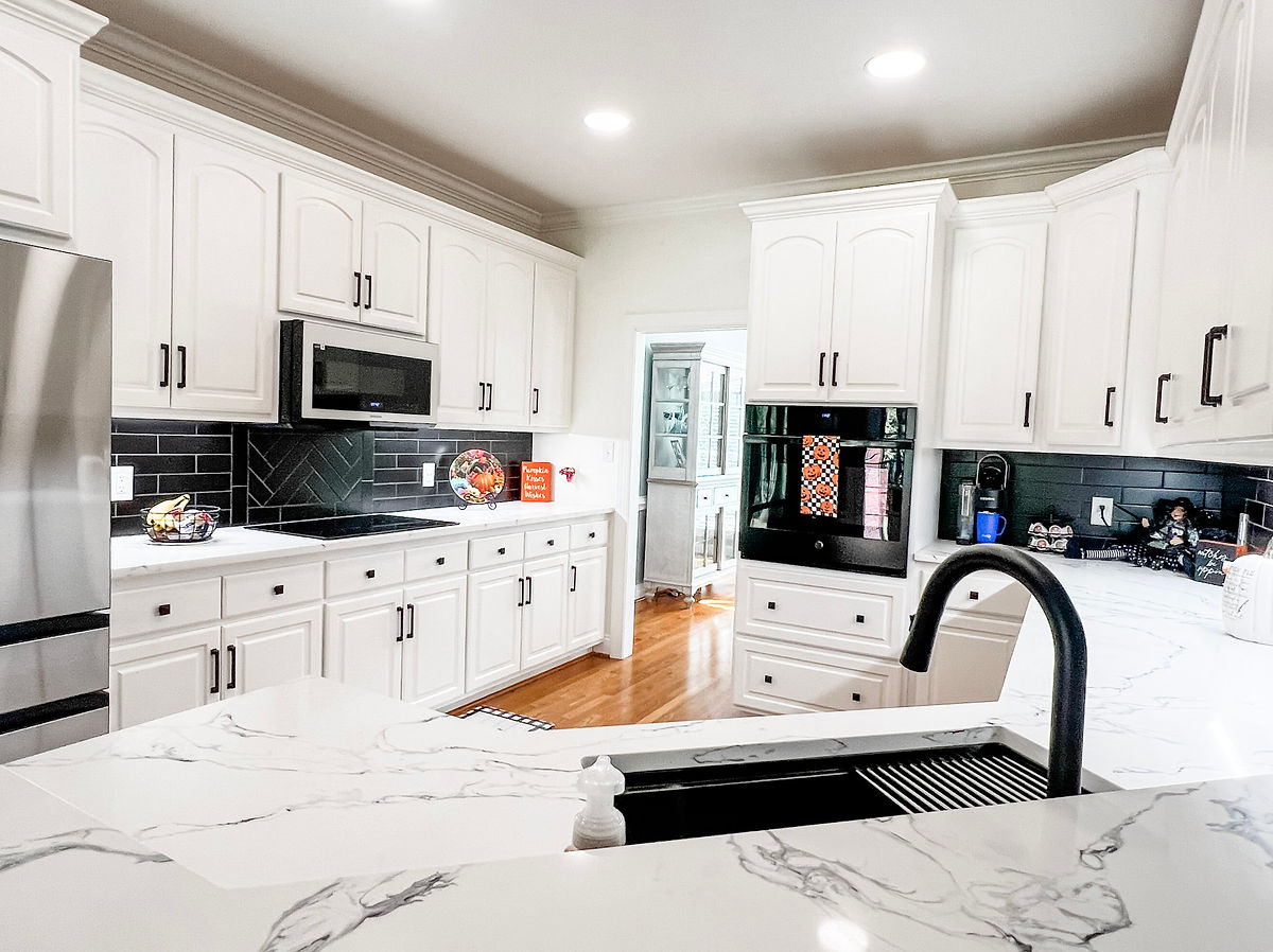 Bright kitchen with white cabinets, black accents, and marble countertops. Includes sink, fruit bowl, and wall sign text 
