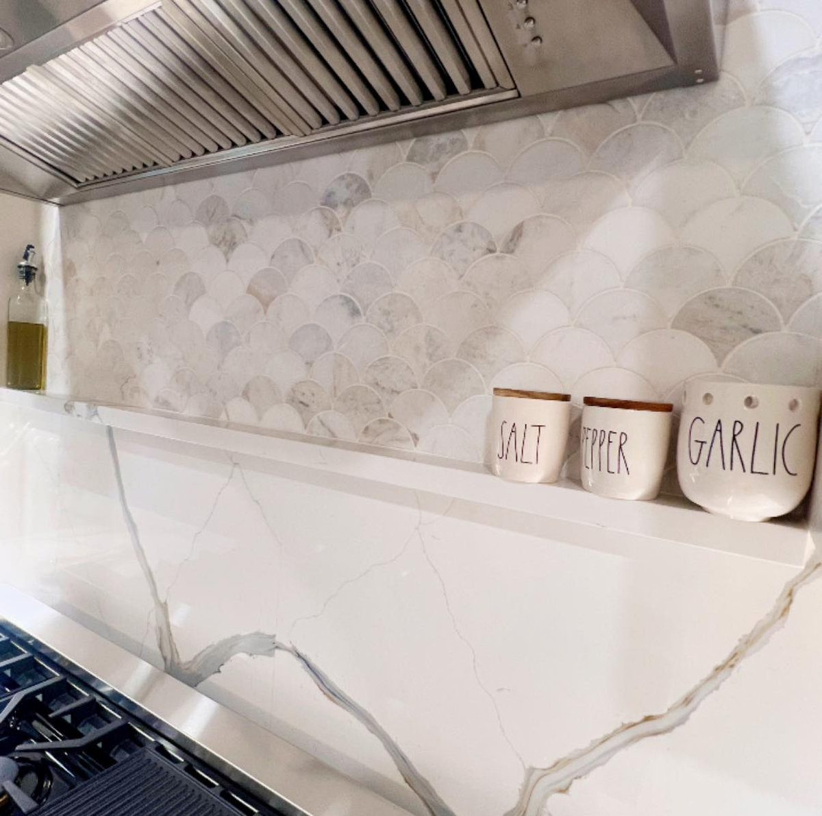 kitchen counter shown behind the range with tiled backsplash and small shelf with jars of spices on it