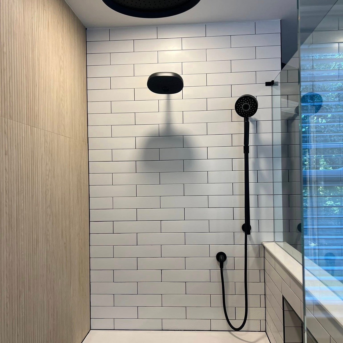 white subway tile shower with a natural tan wall to the left side and black hardware
