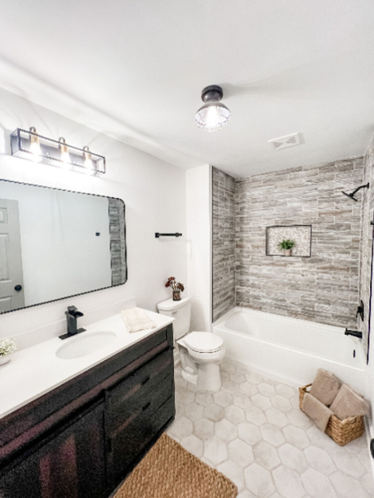 home renovation near Huntersville, NC featuring renovated bathroom with stacked stone look bath tile, hexagon tile flooring, and dark wood vanity.