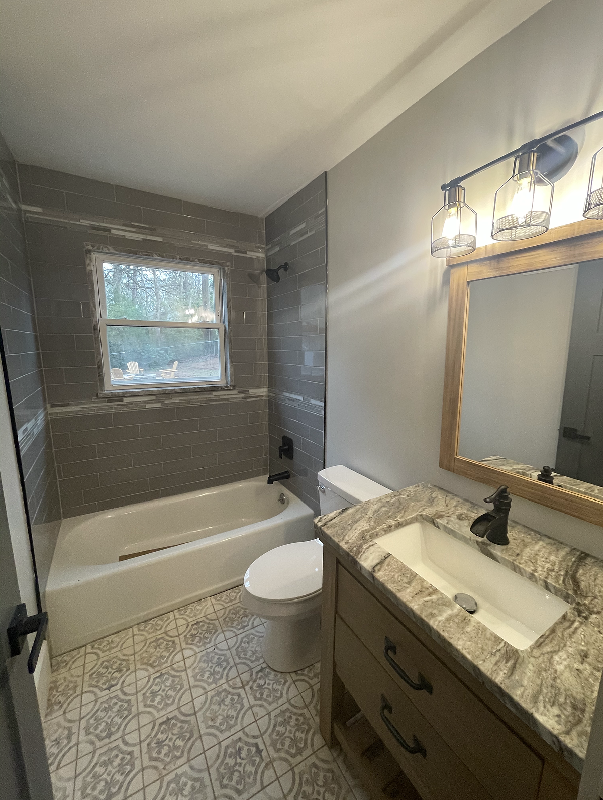 Small renovation of a bathroom with gray decorative tile flooring, granite countertop sink, and retro style light fixture