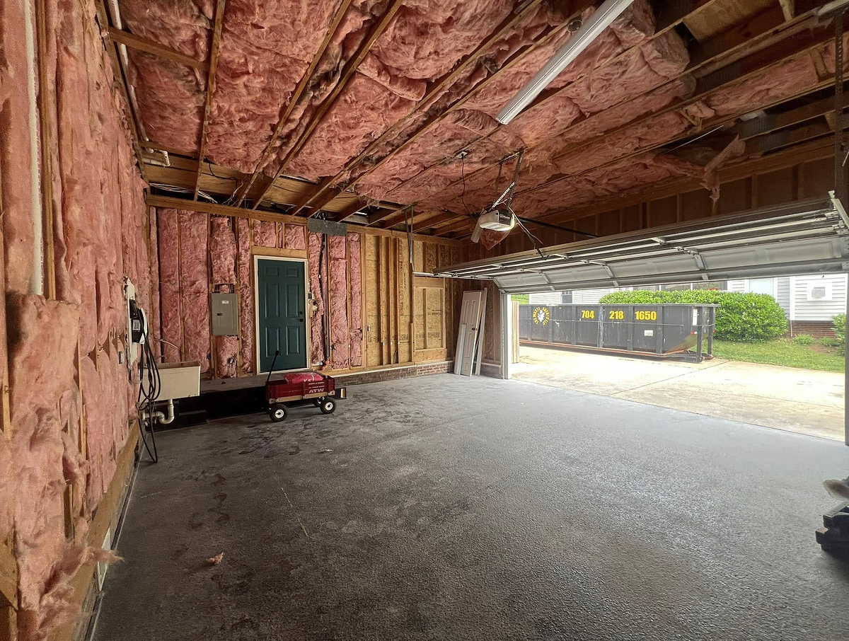 garage conversion before photo showing bare concrete floor, pink insulation lines the walls. part of a home remodel near Cornelius NC.