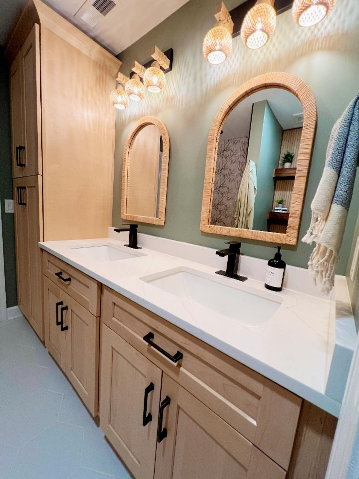 home renovation near Huntersville, NC featuring a bathroom makeover with resort/tropical vibe. Light wood cabinets, natural light fixtures and mirror frames with pale green walls above the sink.