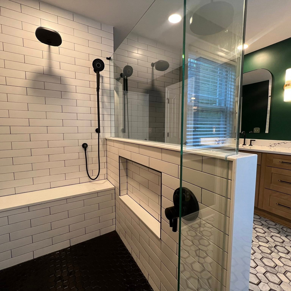 wide view of a dark green bathroom with white subway tiled shower, decoratie marble hex tile flooring, and wooden vanity