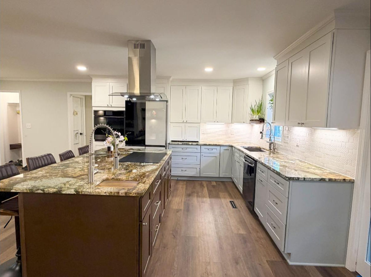 Modern kitchen with marble island, stainless steel sink, and white cabinets. Wooden floors and a plant near the window create a cozy feel.