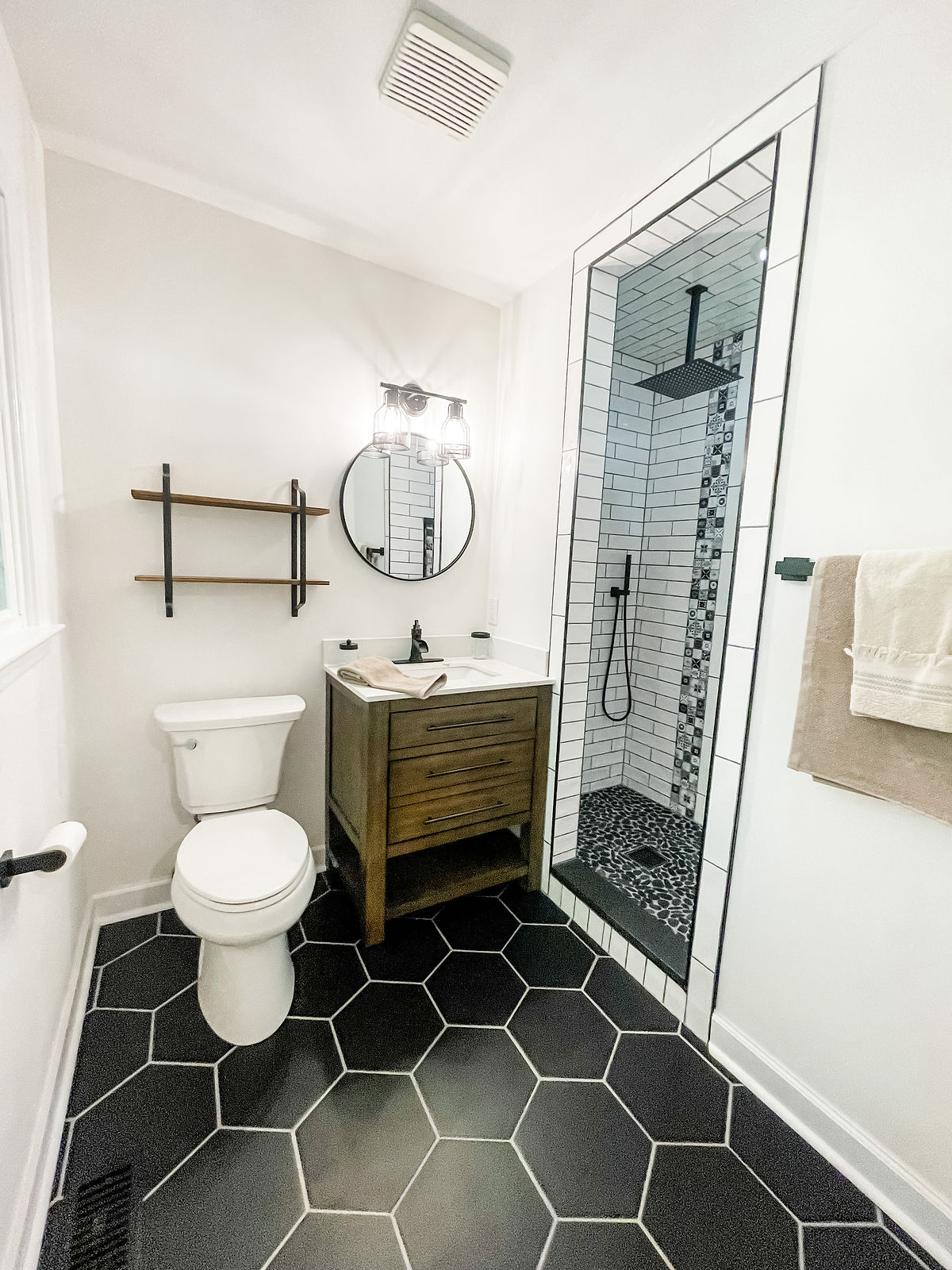 small bathroom renovation featuring black hex tile flooring, wooden vanity, and subway tiled shower stall
