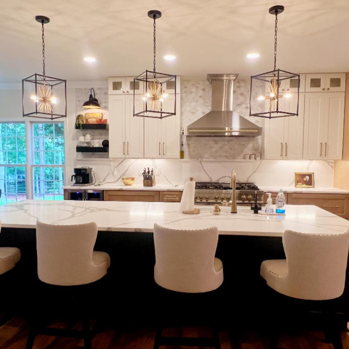light upholstered bar stool  chairs sit at a large island facing an open concept kitchen with some open shelving, some white cabinets, and some wood cabinets