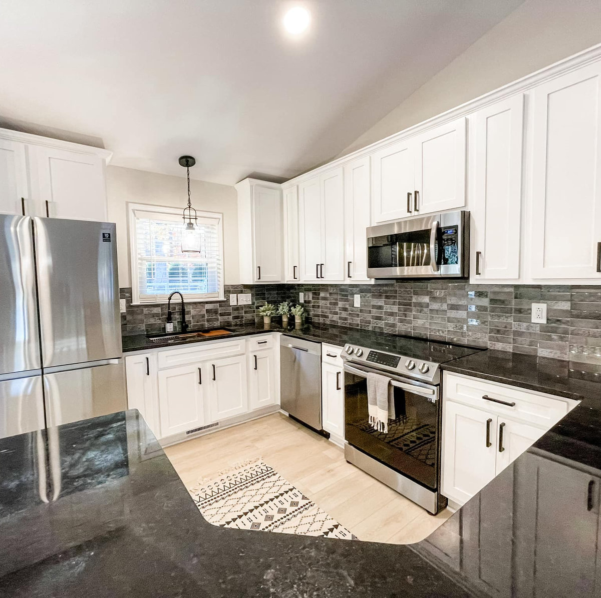 renovated kitchen with dark granite counters, white cabinetry, and light hardwood floors