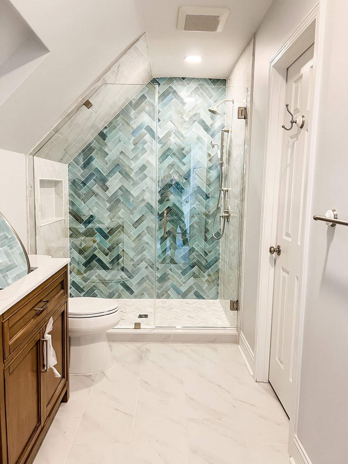 home renovation near Davidson, NC featuring additional bathroom added with green herringbone tiled accent wall, marble flooring, and wooden vanity cabinet.