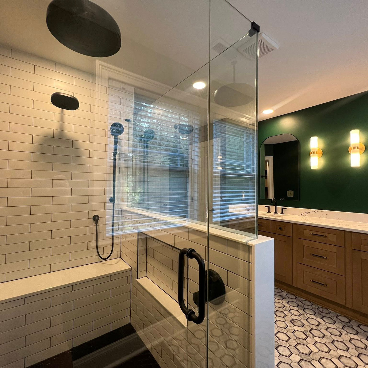 white subway tiled shower with glass walls and door, wooden vanity and dark green wall in the background