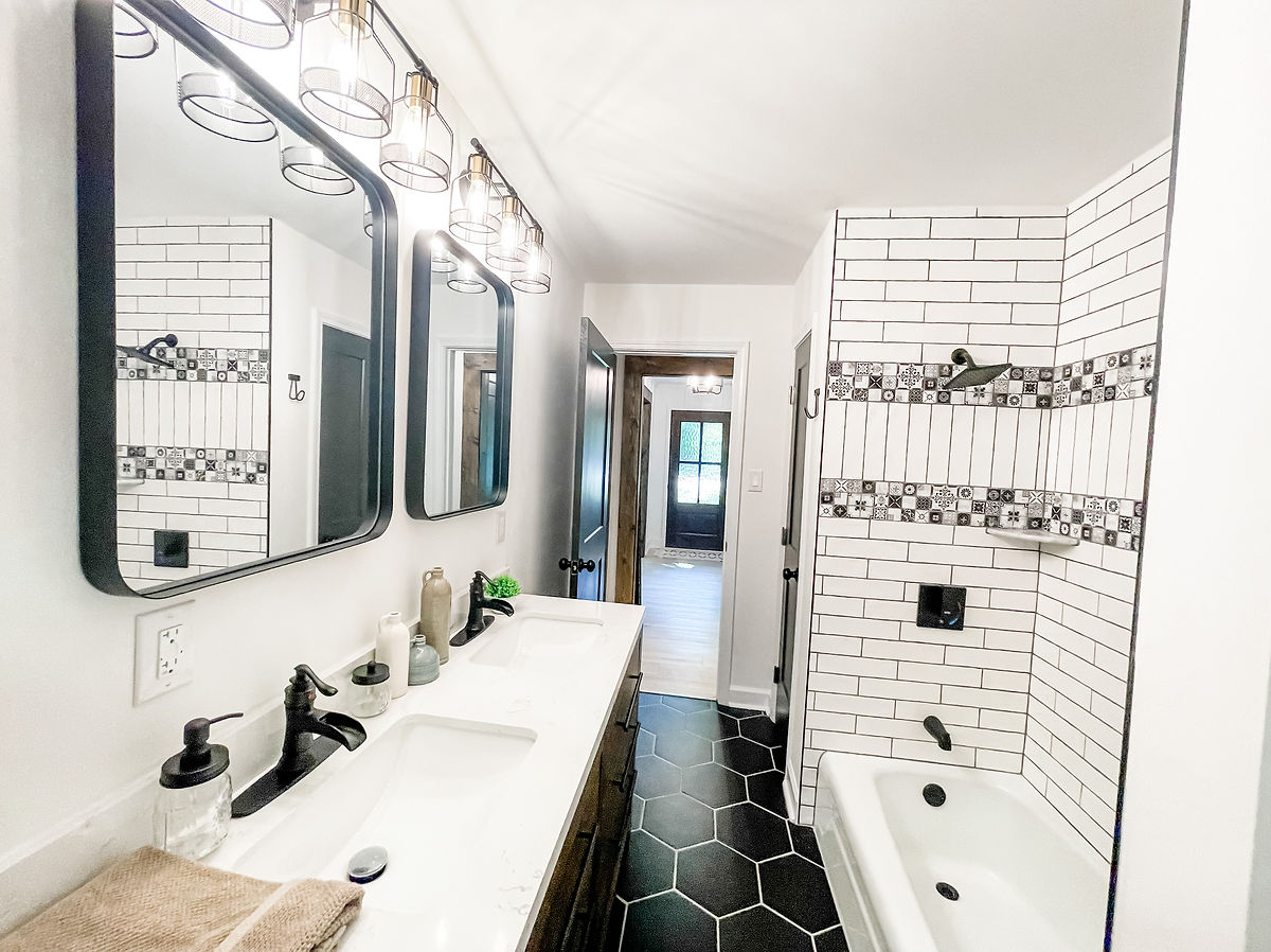 renovated bathroom with black hex tile flooring, white subway tile shower surround, and industrial light fixtures
