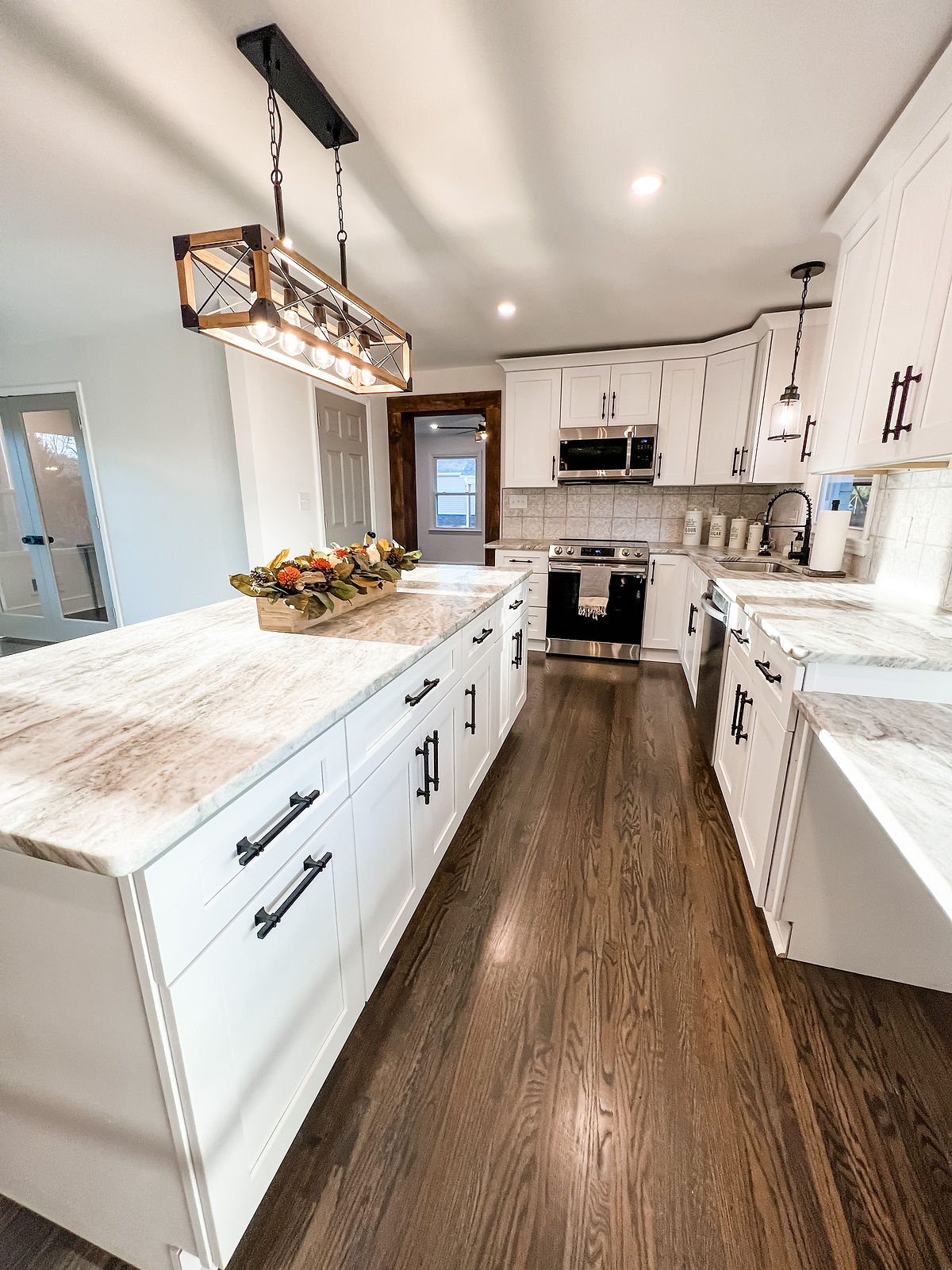 renovated kitchen with gray granite counters, white cabinetry and dark hardware. a large farmhouse light fixture hangs over the island