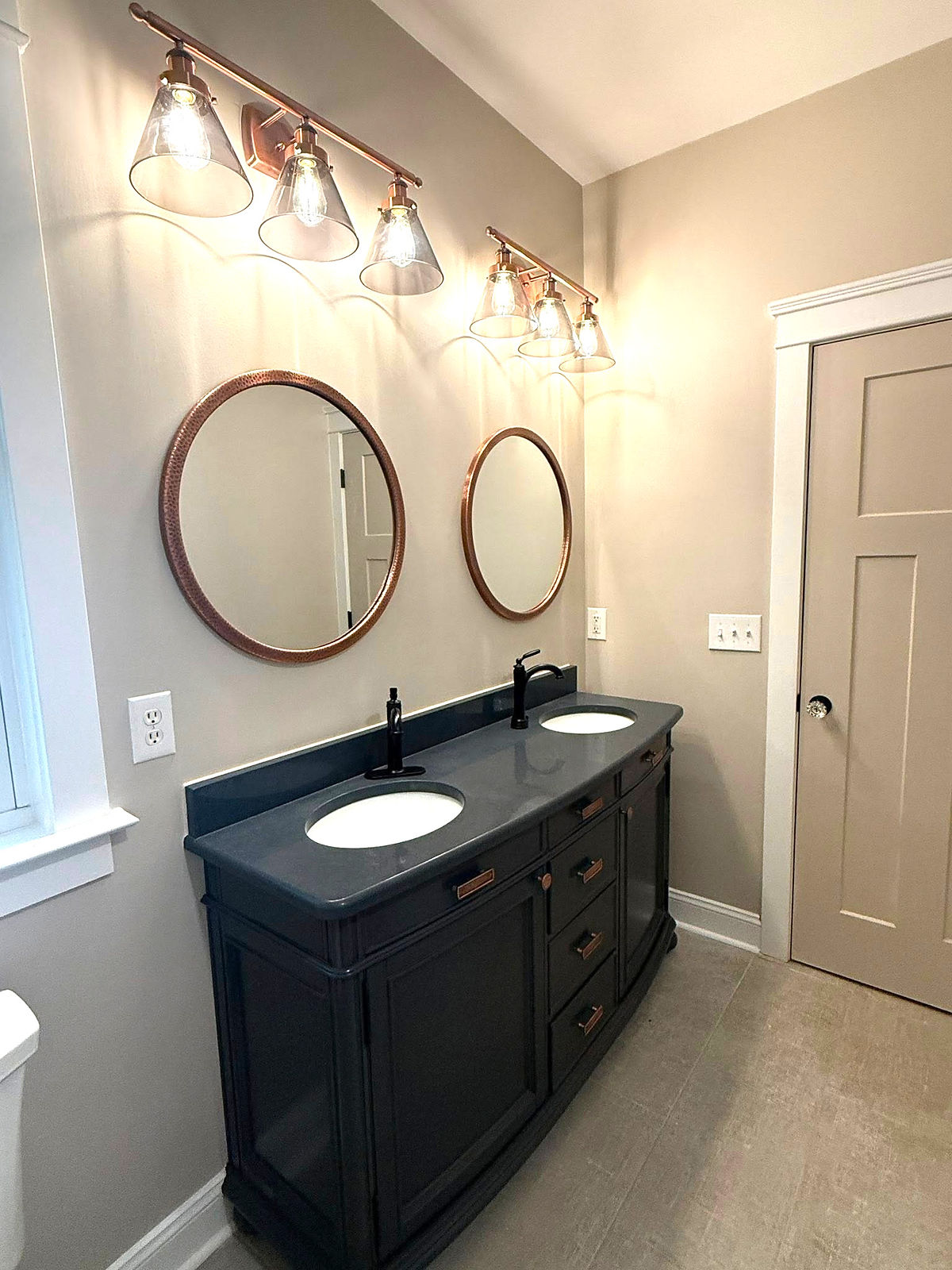home renovation near Huntersville, NC featuring craftsman style bathroom with dark double vanity, round mirrors, and shaded glass light fixtures.