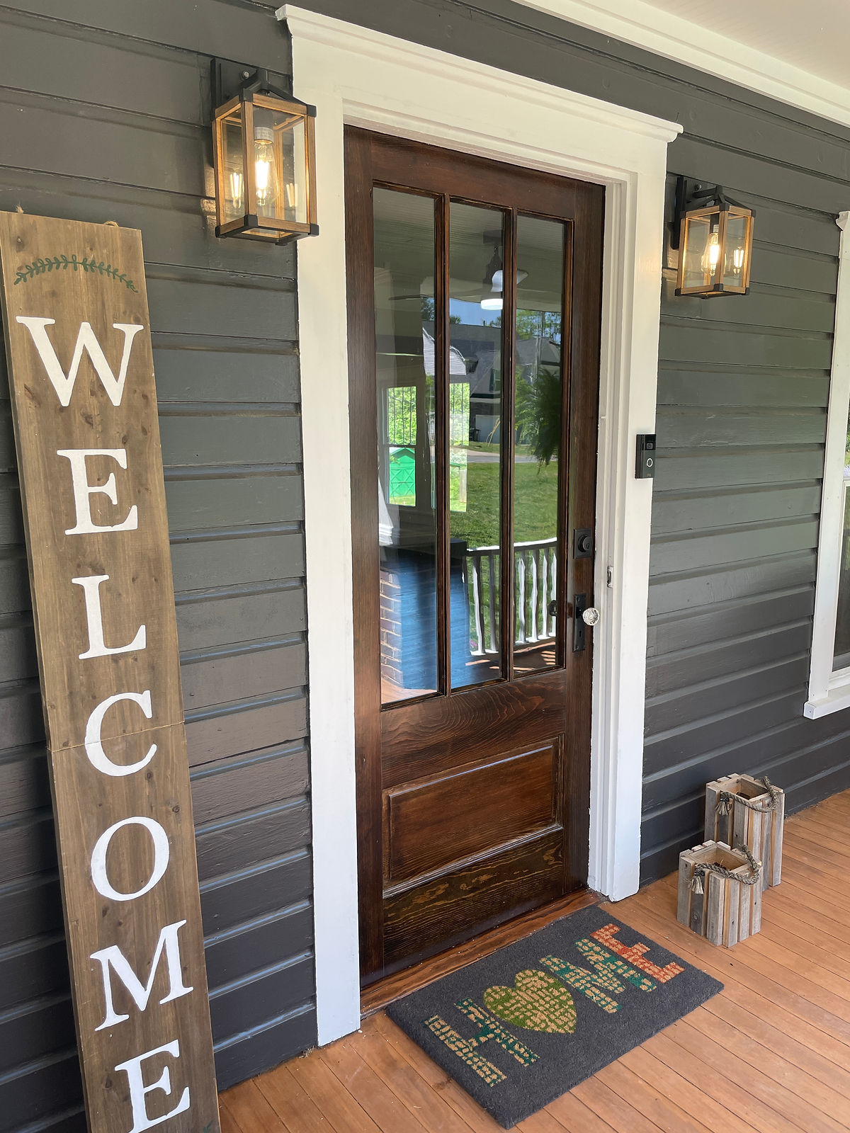 renovated front porch with dark wood siding, wooden floors and door with windows.  A large welcome sign stands to the left of the door.
