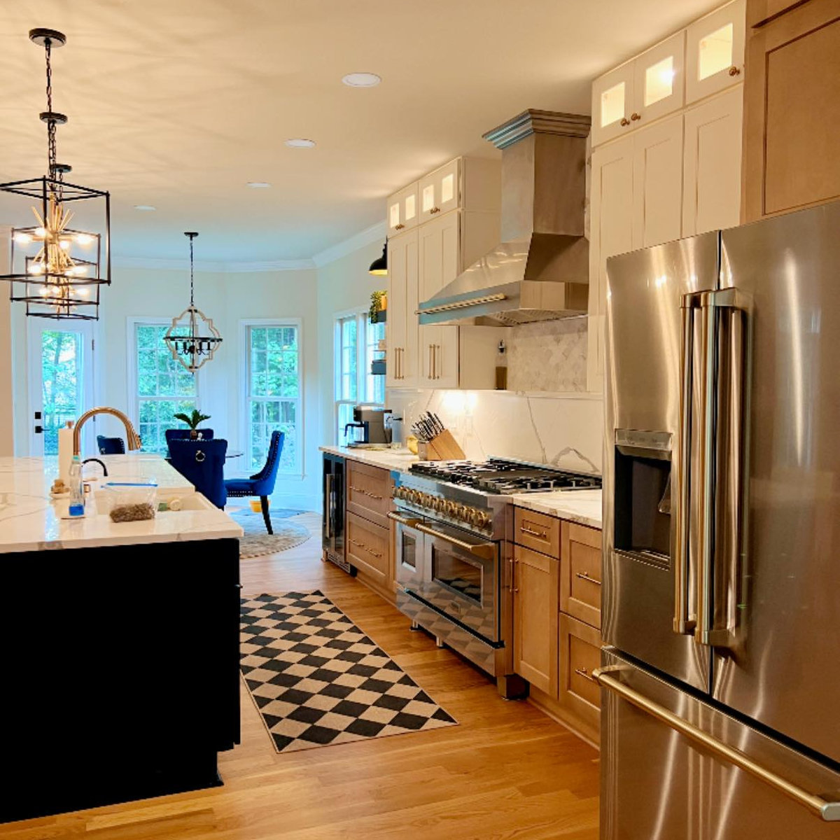 walkway through a renovated kitchen features black, white, and wood cabinets, a black checkered rug, and gold hardware