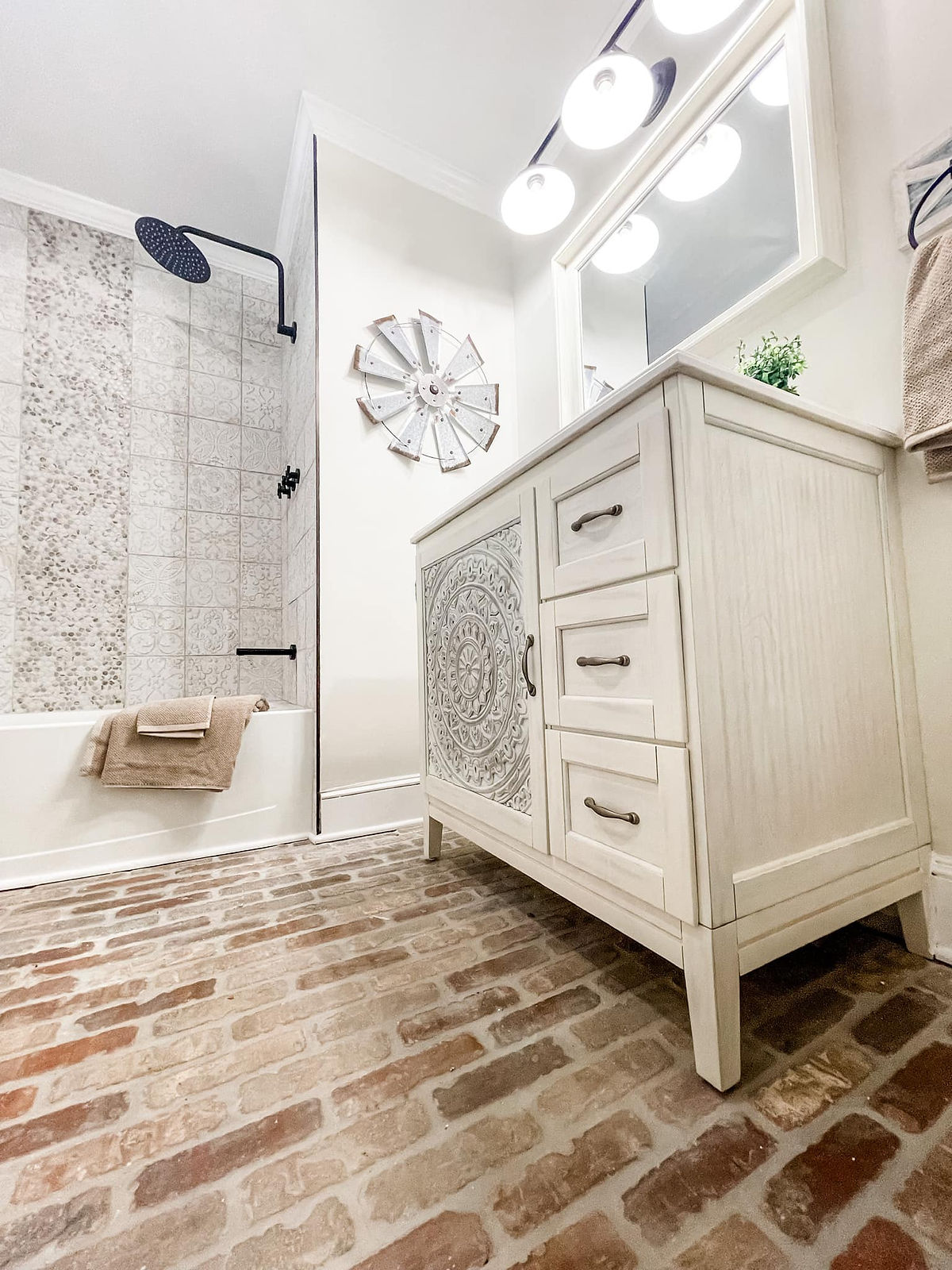 Angled shot of a home renovation near Cornelius, NC featuring a renovated guest bathroom. Bathroom includes brick flooring, tiled shower insert, and decorative vanity.