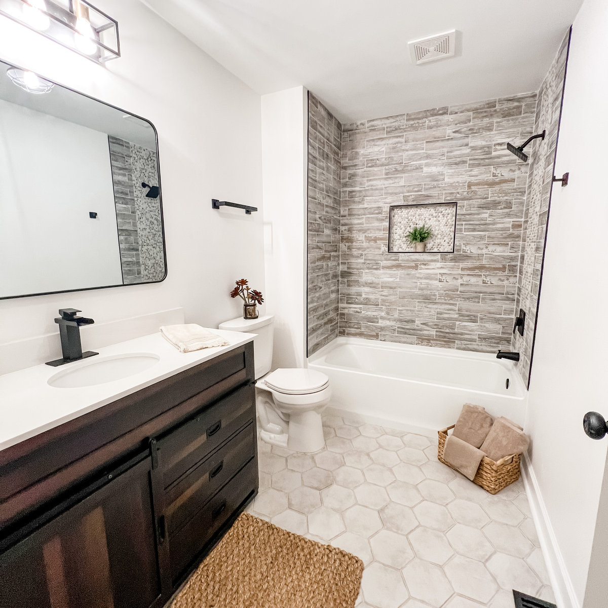 renovated bathroom with hex tile flooring, gray tiled tub surround, and a dark wood vanity