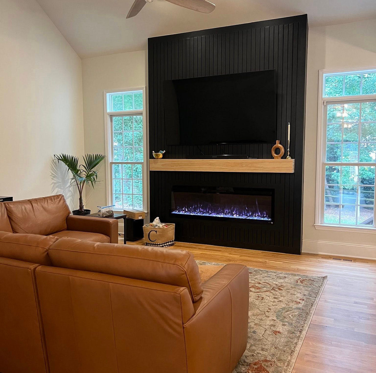 wide view of living room from behind a light leather couch facing the black media accent wall between two windows