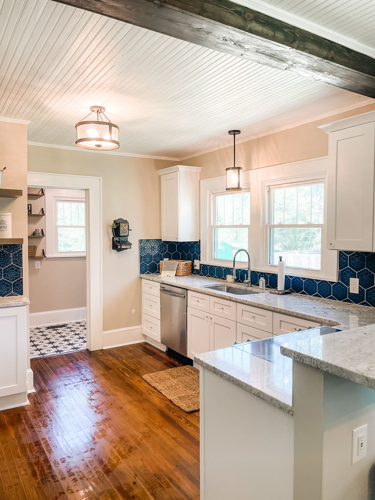 renovated kitchen with refinished floors, white cabinetry, and dark blue tile backsplash