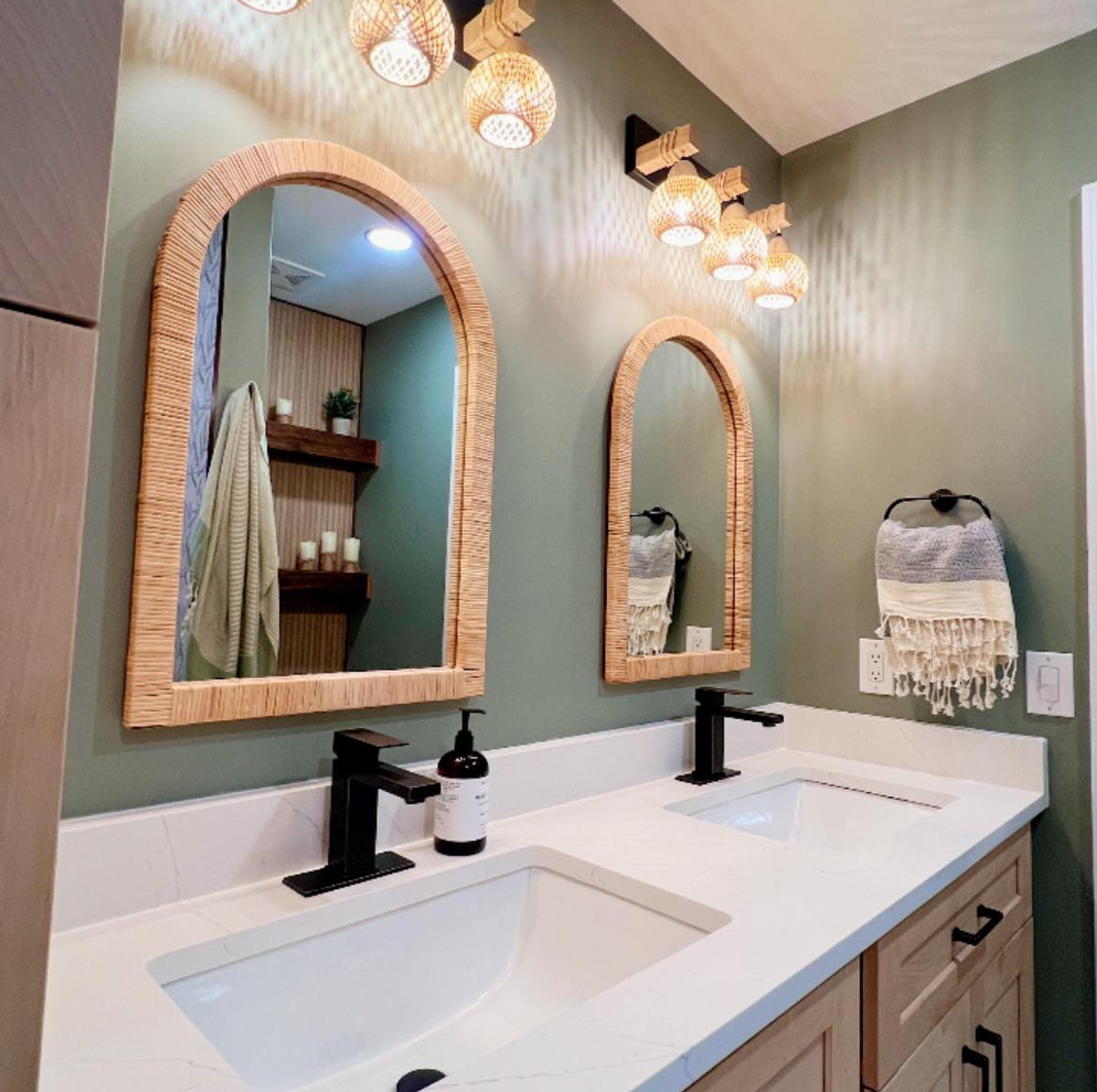 white bathroom counters with double sinks in a wooden vanity. green walls and natural wood frames behind the sinks