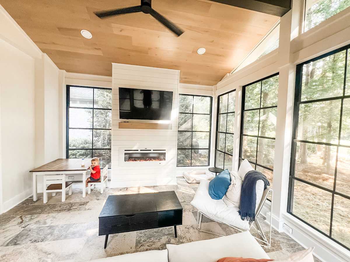 remodeled sun room with large modern windows, tv mounted above fireplace, and tiled floors