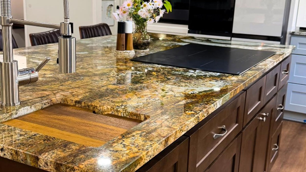 Stylish kitchen with granite island, sleek faucet, and stovetop. Vase of flowers adds a touch of color. Modern cabinets and wood floor.