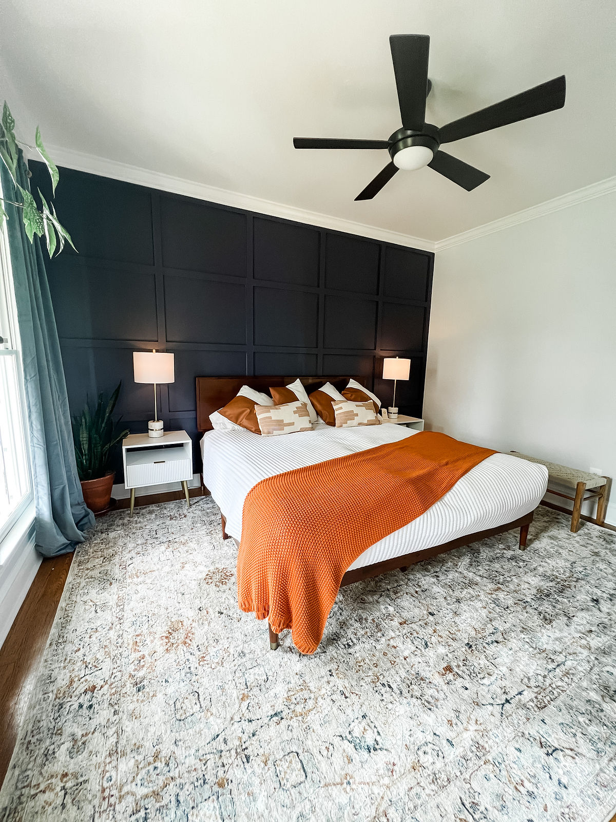 bold creative bedroom home remodel near Huntersville, NC featuring a dark blue accent wall, orange bedding, and an eclectic rug