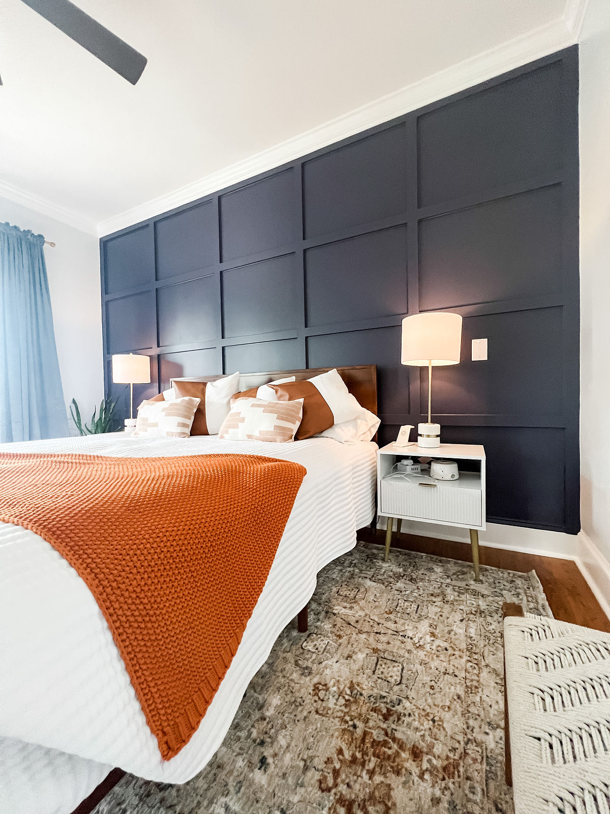home renovation near Davidson, NC featuring renovated guest room with dark paneled accent wall, vintage rug, and white bed with orange throw blanket