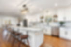 renovated kitchen by two chicks homes. Kitchen features white cabinetry, wood floors, and stone counters