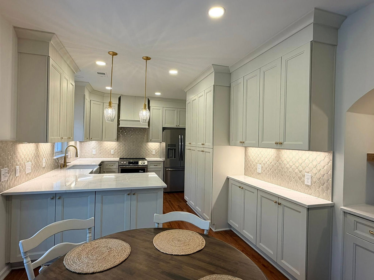 Spacious kitchen with white cabinets, pendant lights, and a round table. Textured backsplash adds elegance. Bright, modern ambiance.