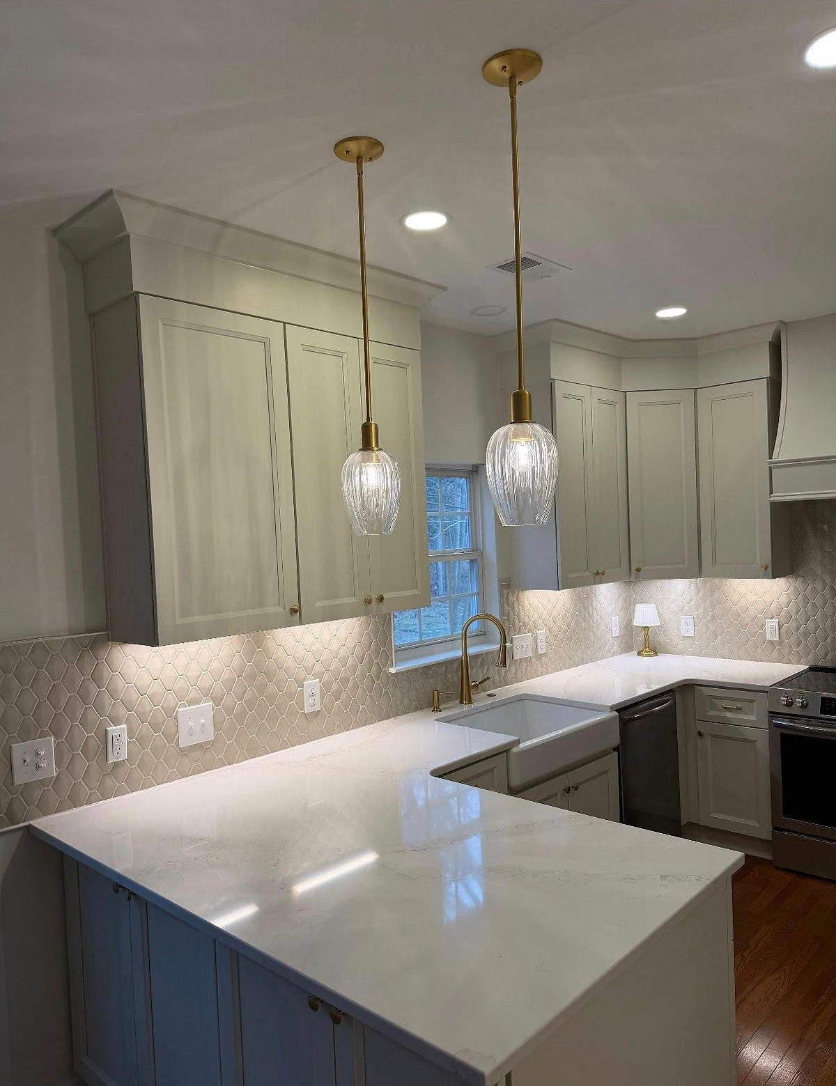 Modern kitchen with white cabinets, quartz countertops, gold pendant lights, and diamond-patterned backsplash. Bright and elegant design.