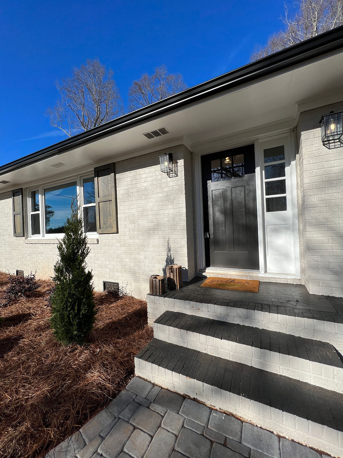 renovated house exterior with painted brick, dark wood door, and paver walkway