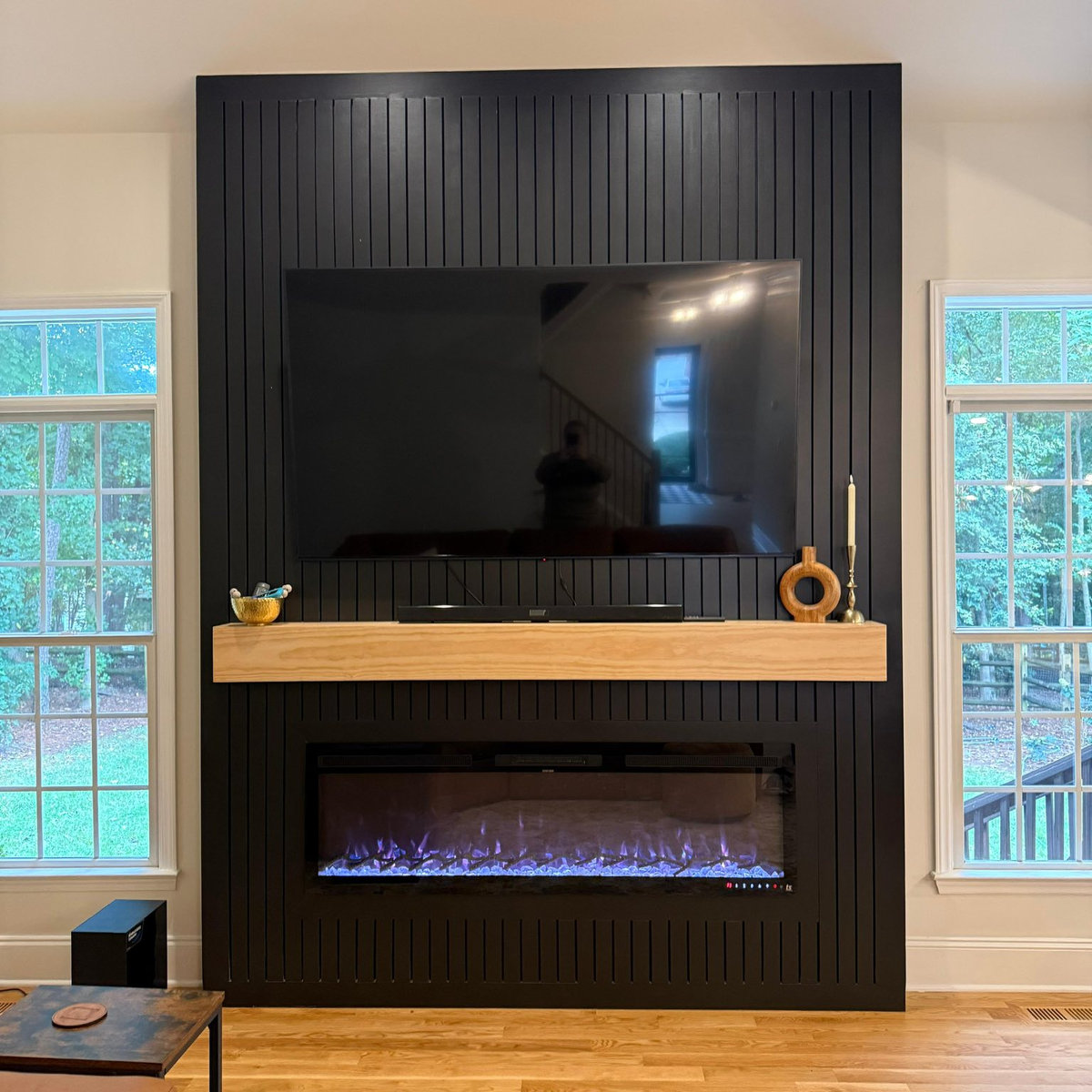 statement black media wall with large tv, modern wood mantel, and electric fireplace built in beneath
