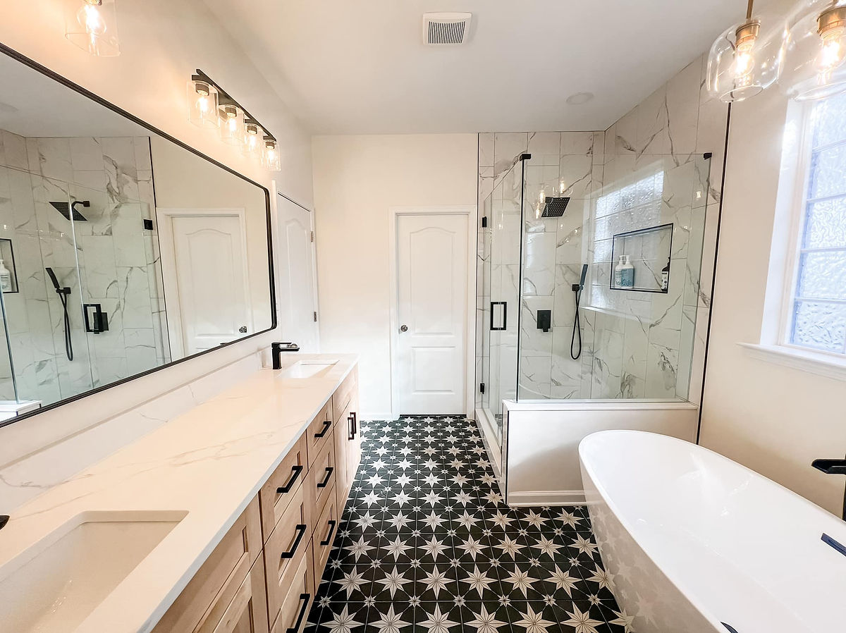 home renovation near cornelius NC featuring a new bathroom with black and white decorative tile flooring. There is a marble shower stall at the far right of the room, a light wood double vanity to the left and a large soaking tub at the front right.