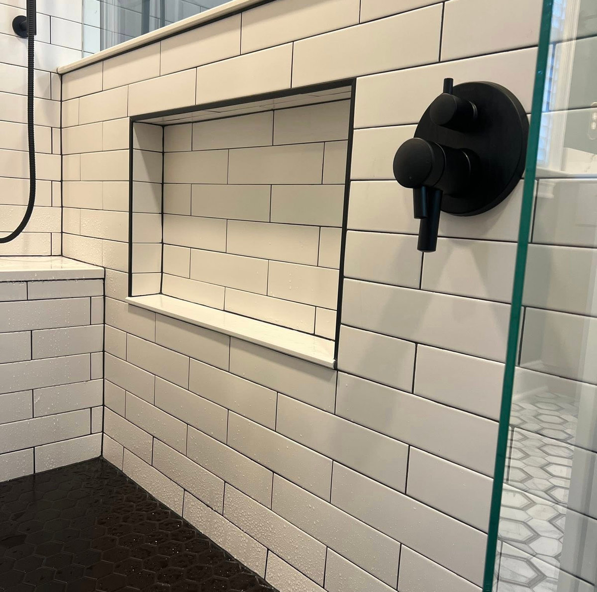 white subway tiled shower with black flooring and black hardware