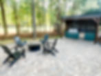 exterior home renovation near Cornelius, NC. Wooded lot features brick paver patio, Adirondack chairs around a fire pit, and outdoor kitchen.