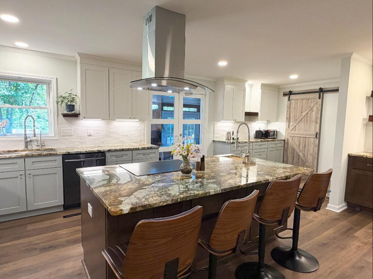 Modern kitchen with marble island, four barstools, stainless steel appliances, light gray cabinets, and a sliding barn door. Bright and spacious.