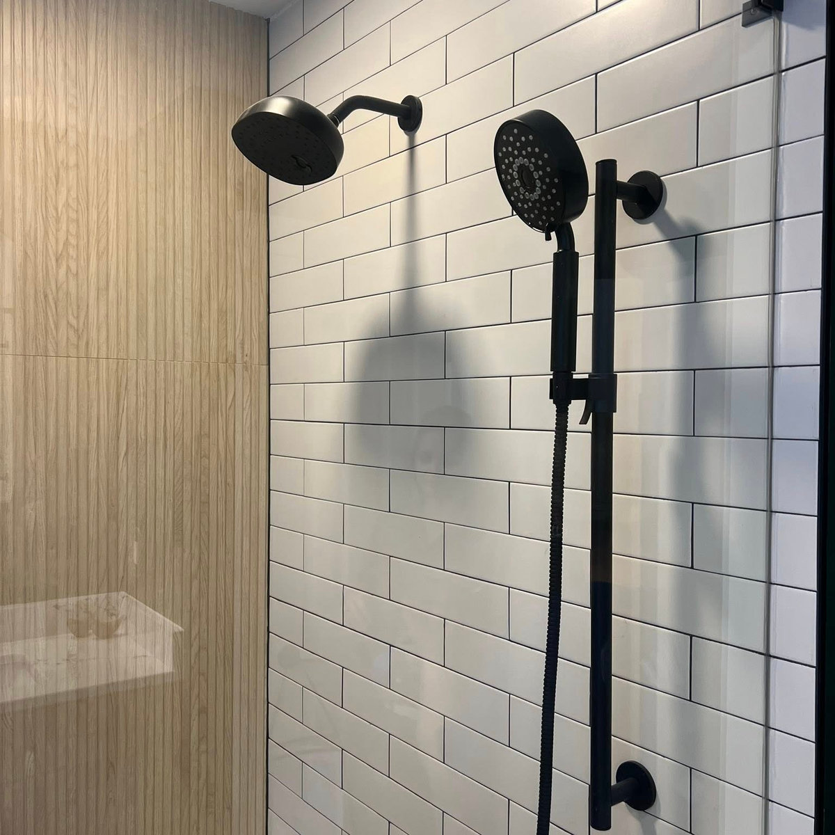 white subway tiled shower with black hardware and wood look wall in the back