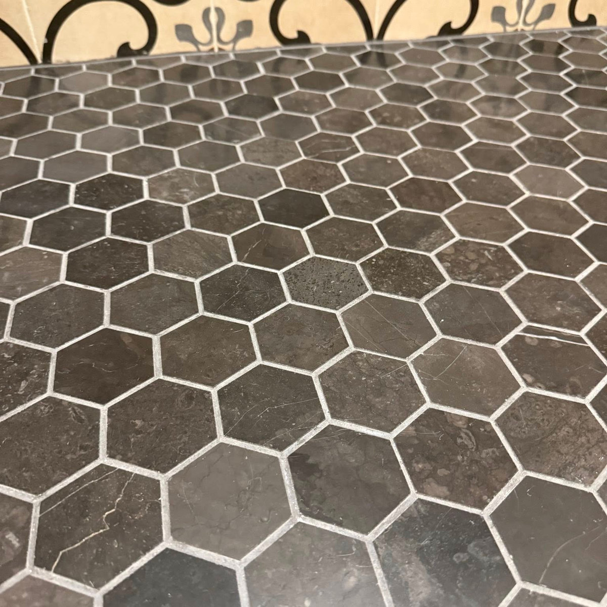 dark gray hex tile flooring meets a decorative brown and blue painted tile wall
